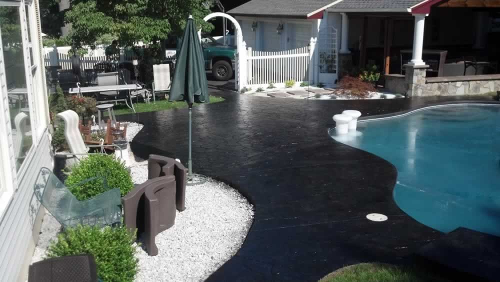 Backyard pool and patio with black walkway, white gravel, chairs, and a closed umbrella