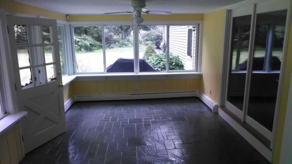 Empty sunroom with yellow walls, dark tile floor, and large windows overlooking greenery