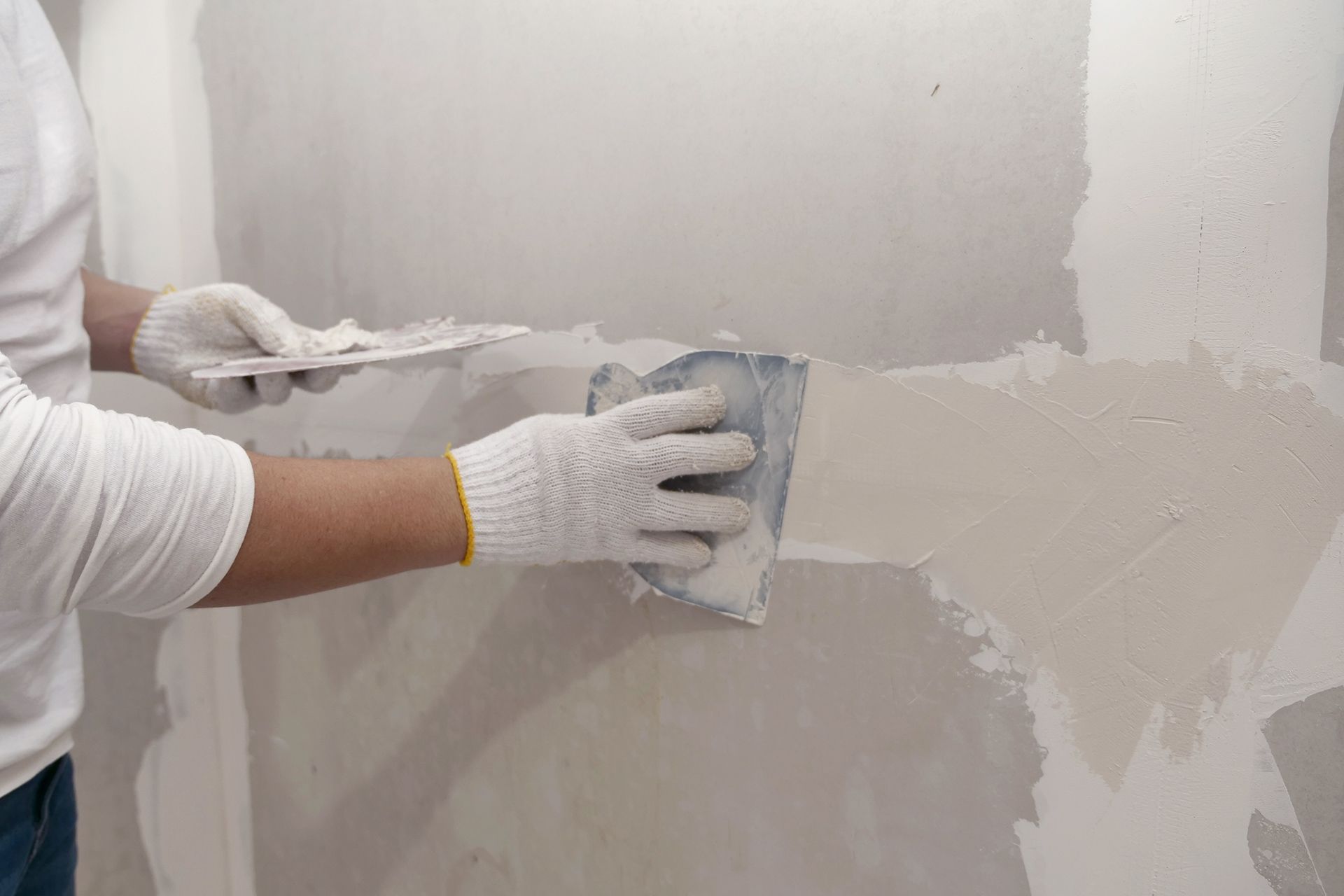 Person smoothing gray wall plaster with a trowel during drywall repair