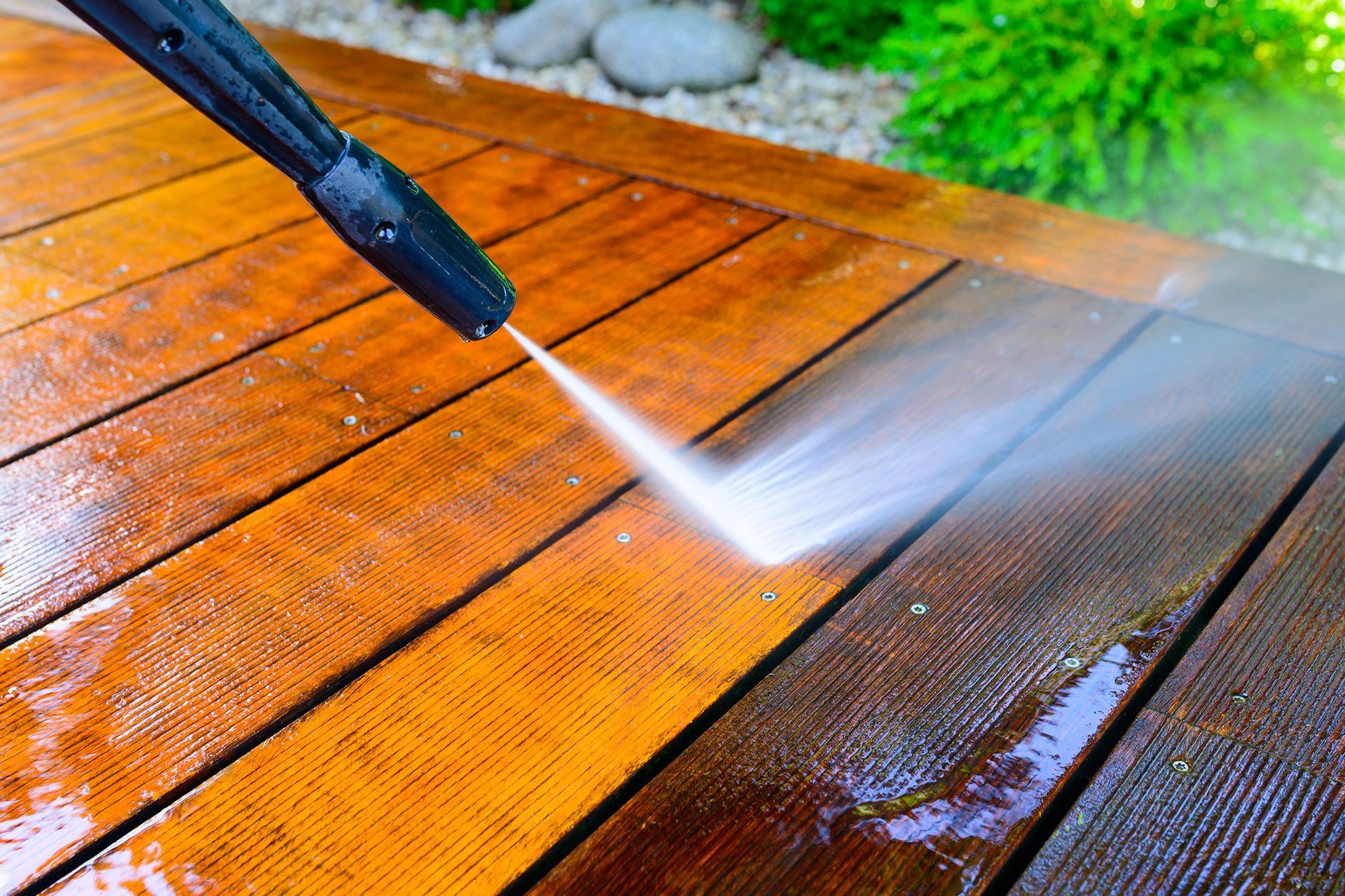 Pressure washing a wet wooden deck, spraying water across orange-brown boards
