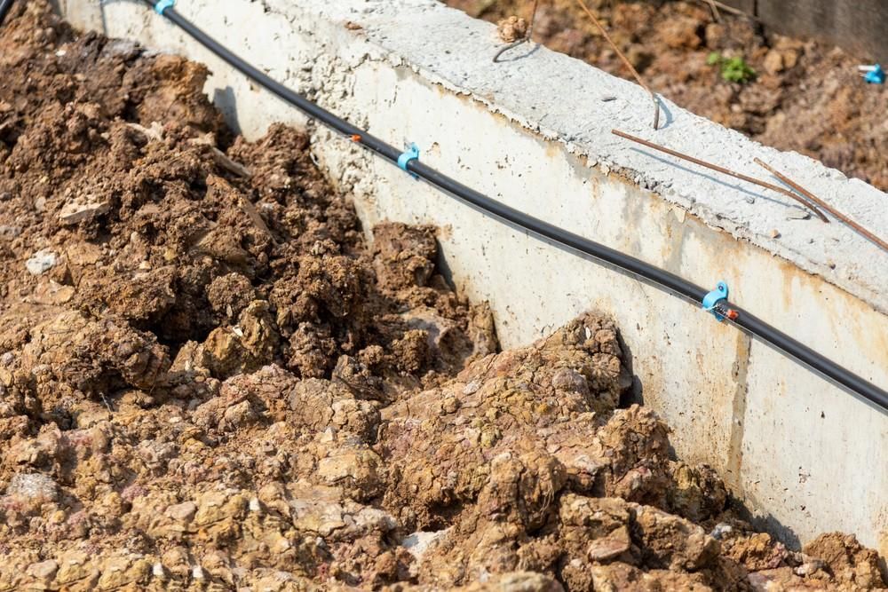 A concrete foundation with a black pipe attached, surrounded by soil.