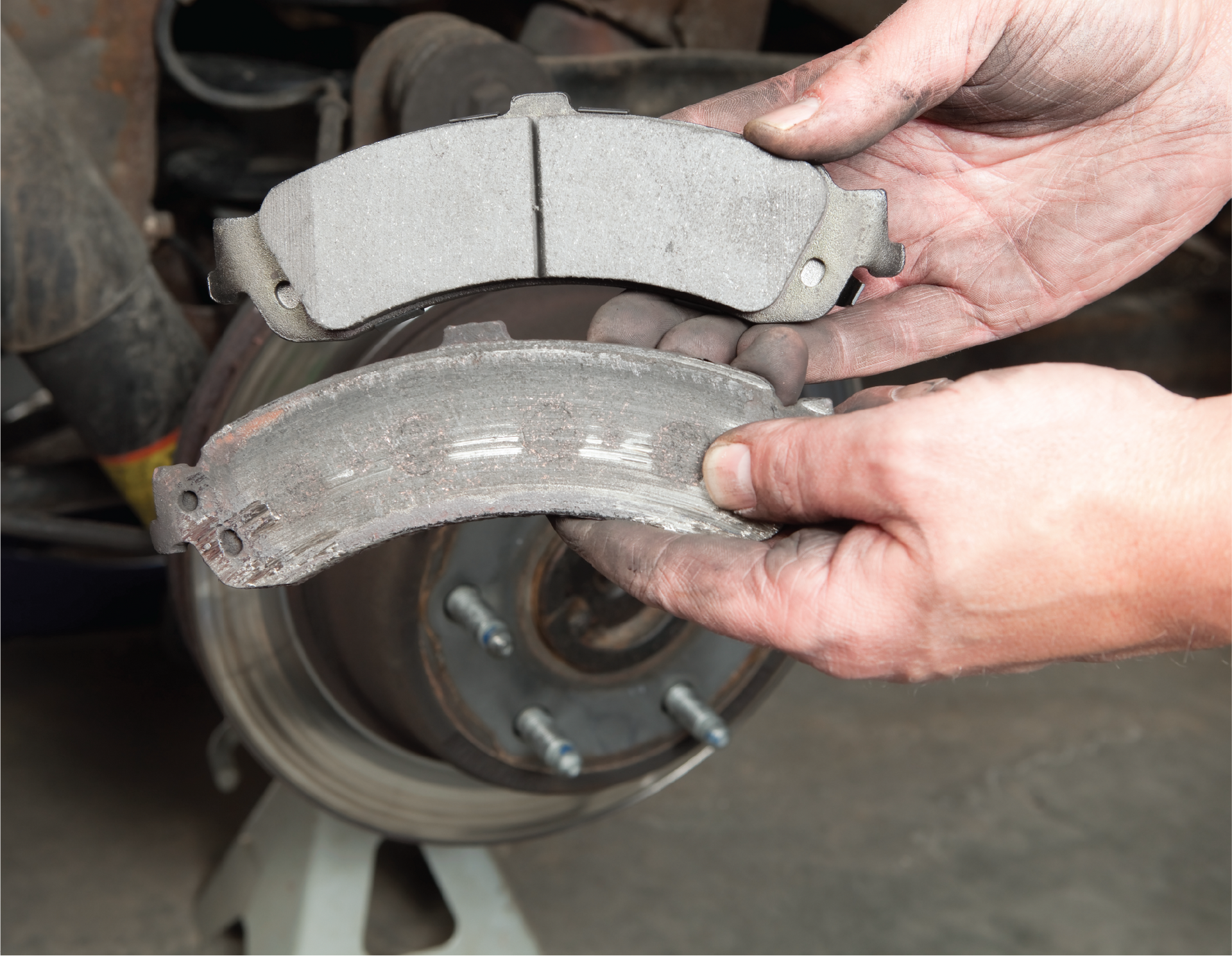 A person is holding a brake pad in front of a car.