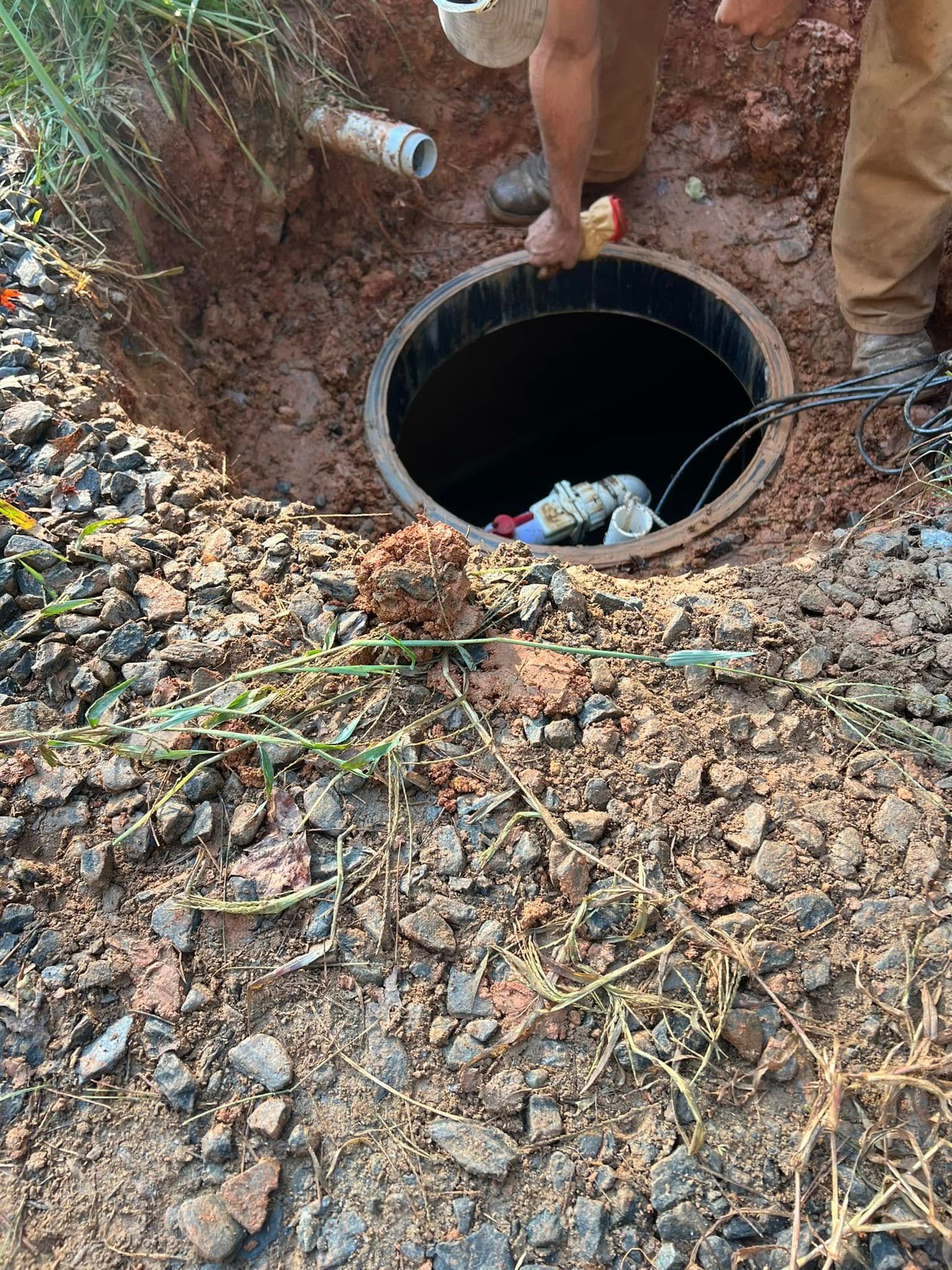 A man is standing next to a septic tank in the dirt.