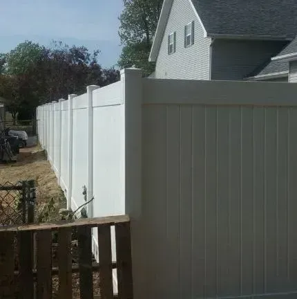 White vinyl privacy fence along a suburban yard beside a house, with a wooden gate in the foreground