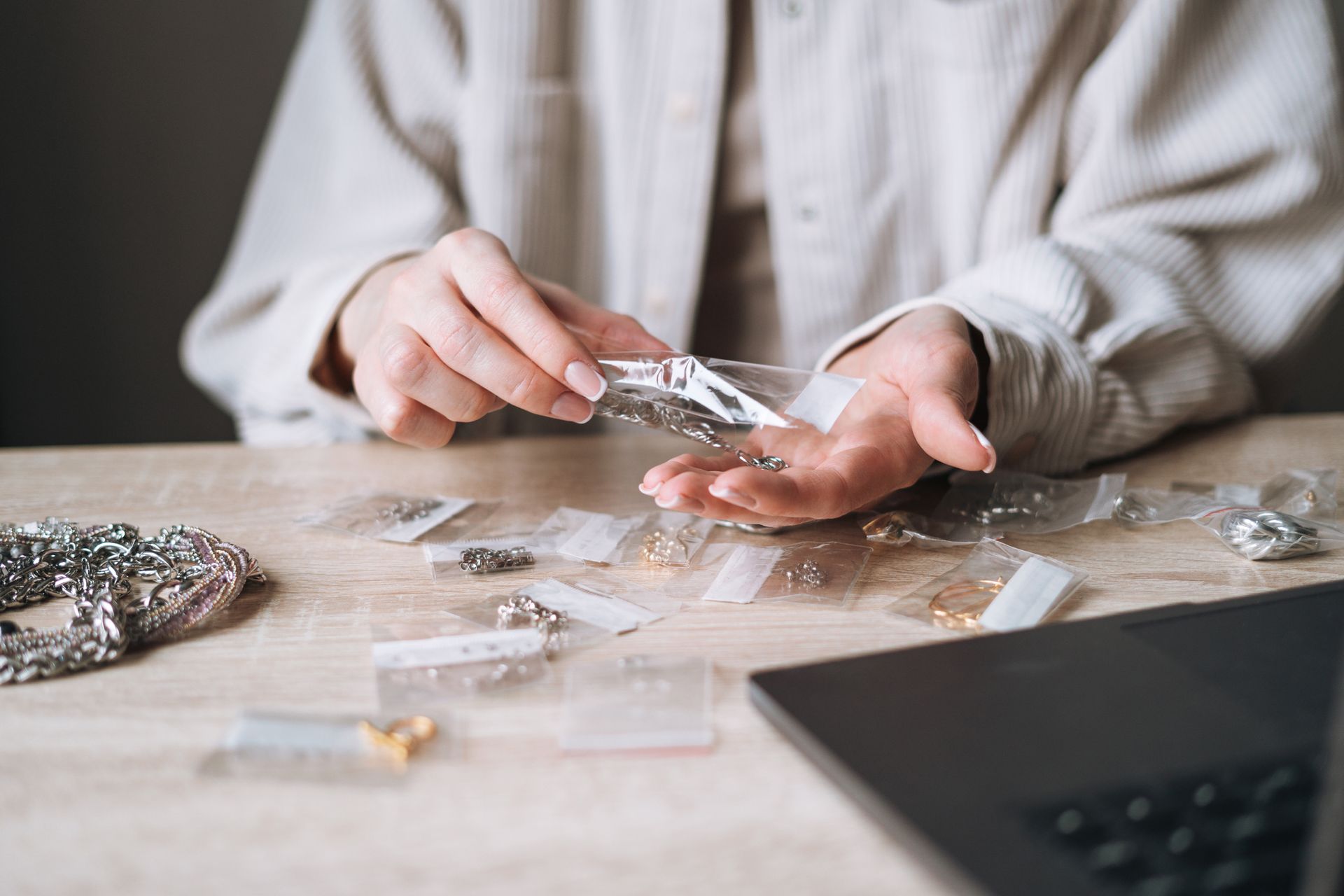Young woman jewelry designer creating items and working with laptop at table in the studio.