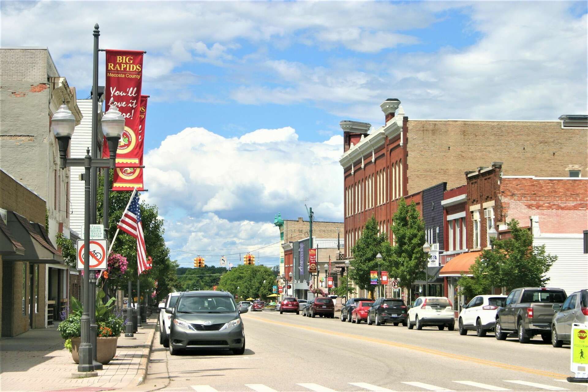 Downtown street with cars, buildings, flags, and cloudy sky.