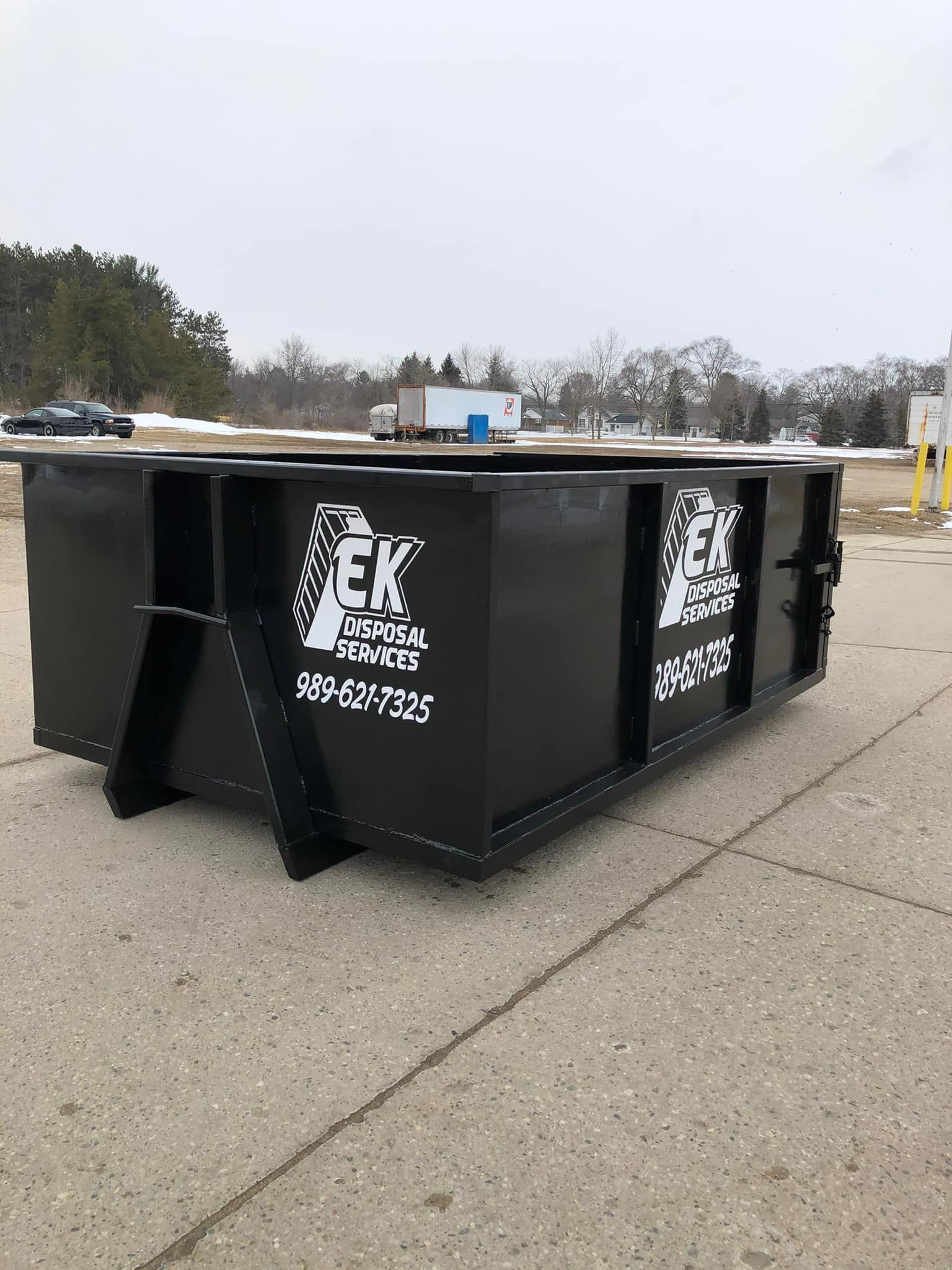Two workers in orange vests and brown pants emptying trash into a dumpster on a residential street.