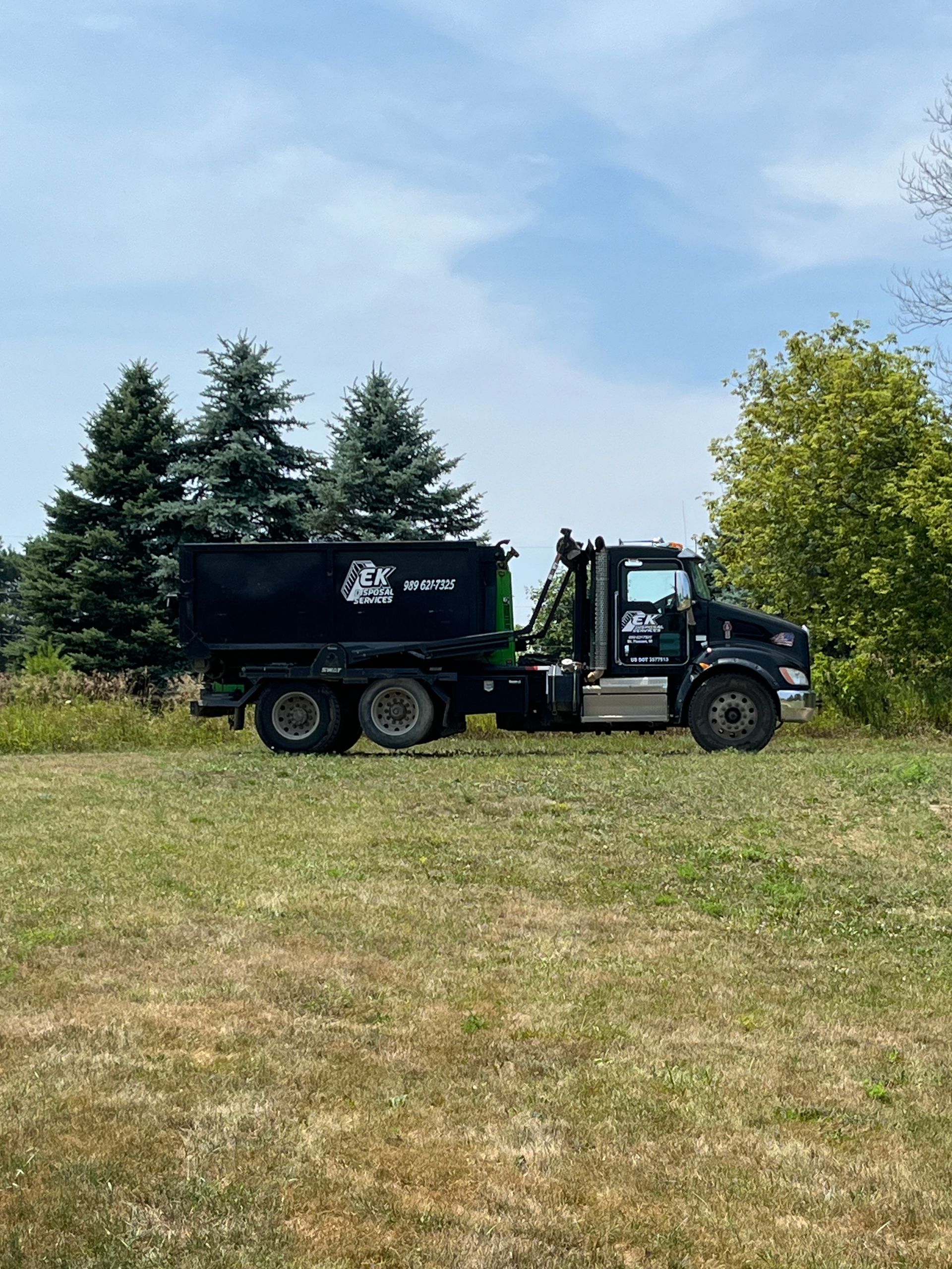 Gray dumpster filled with yard waste on a residential street in front of a two-story house.