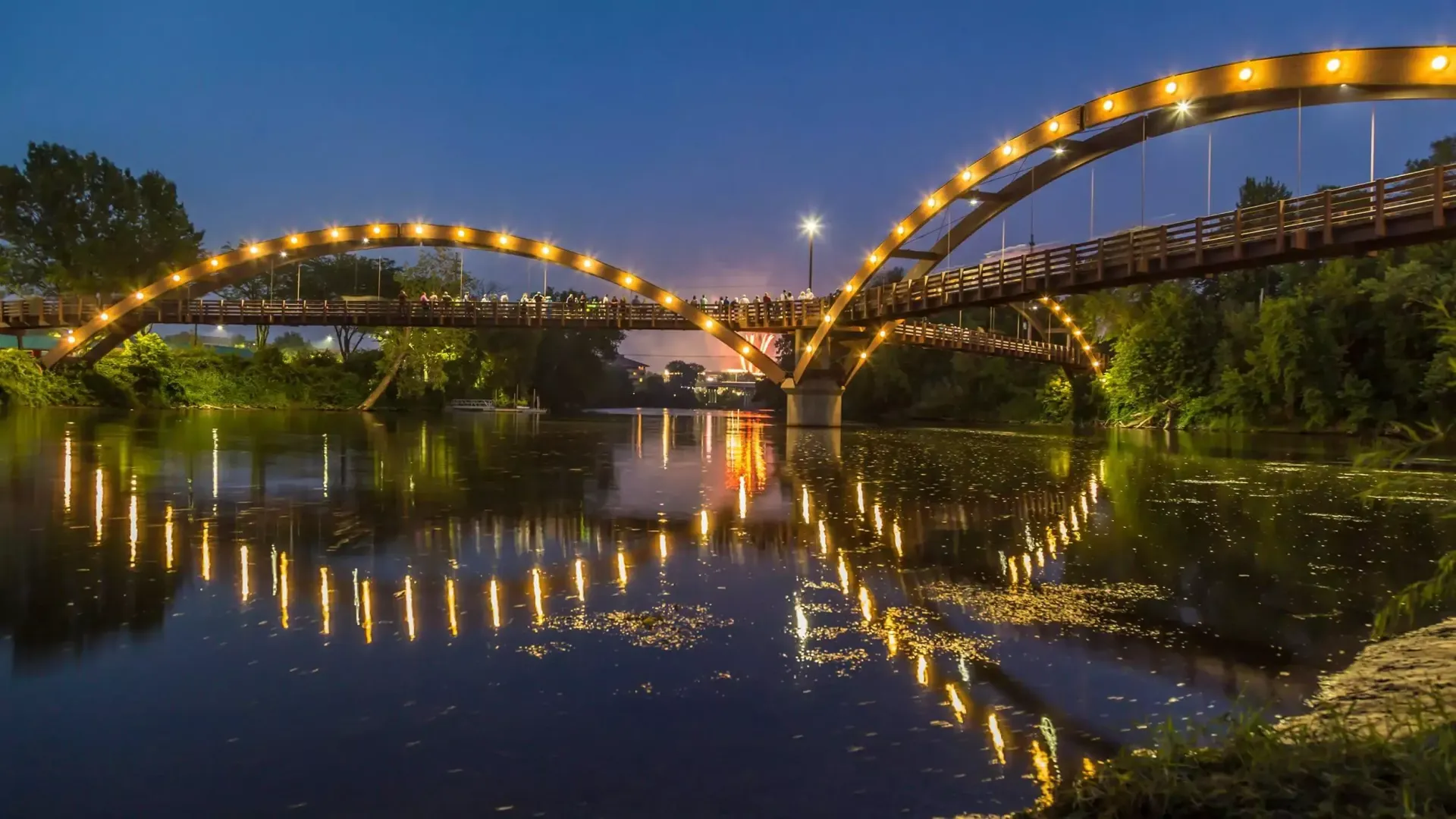 Bridge over water at night, arched with strings of lights reflected in the water.