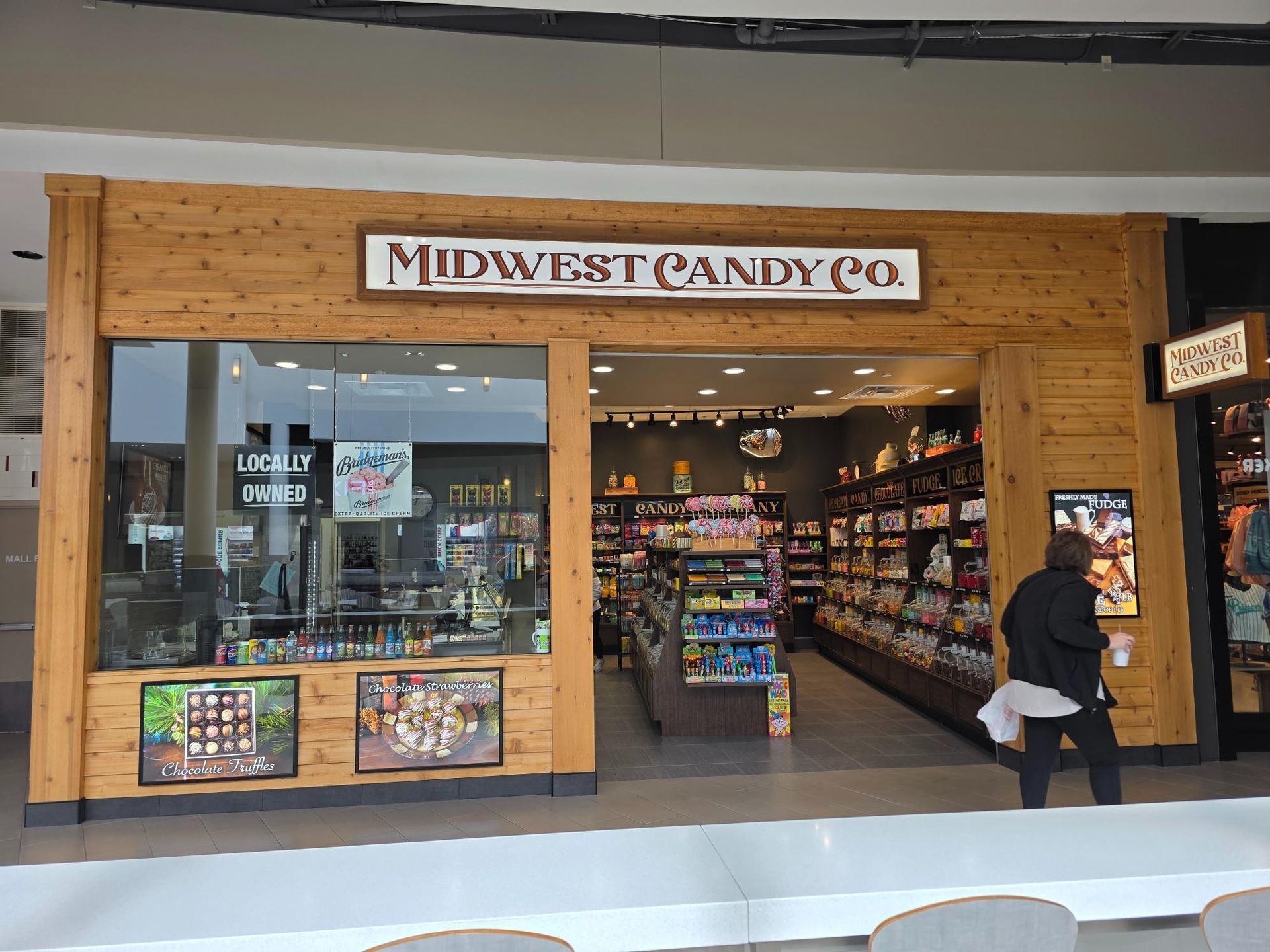 Midwest Candy Co. store front in a mall. A person walks in front. Wooden exterior.