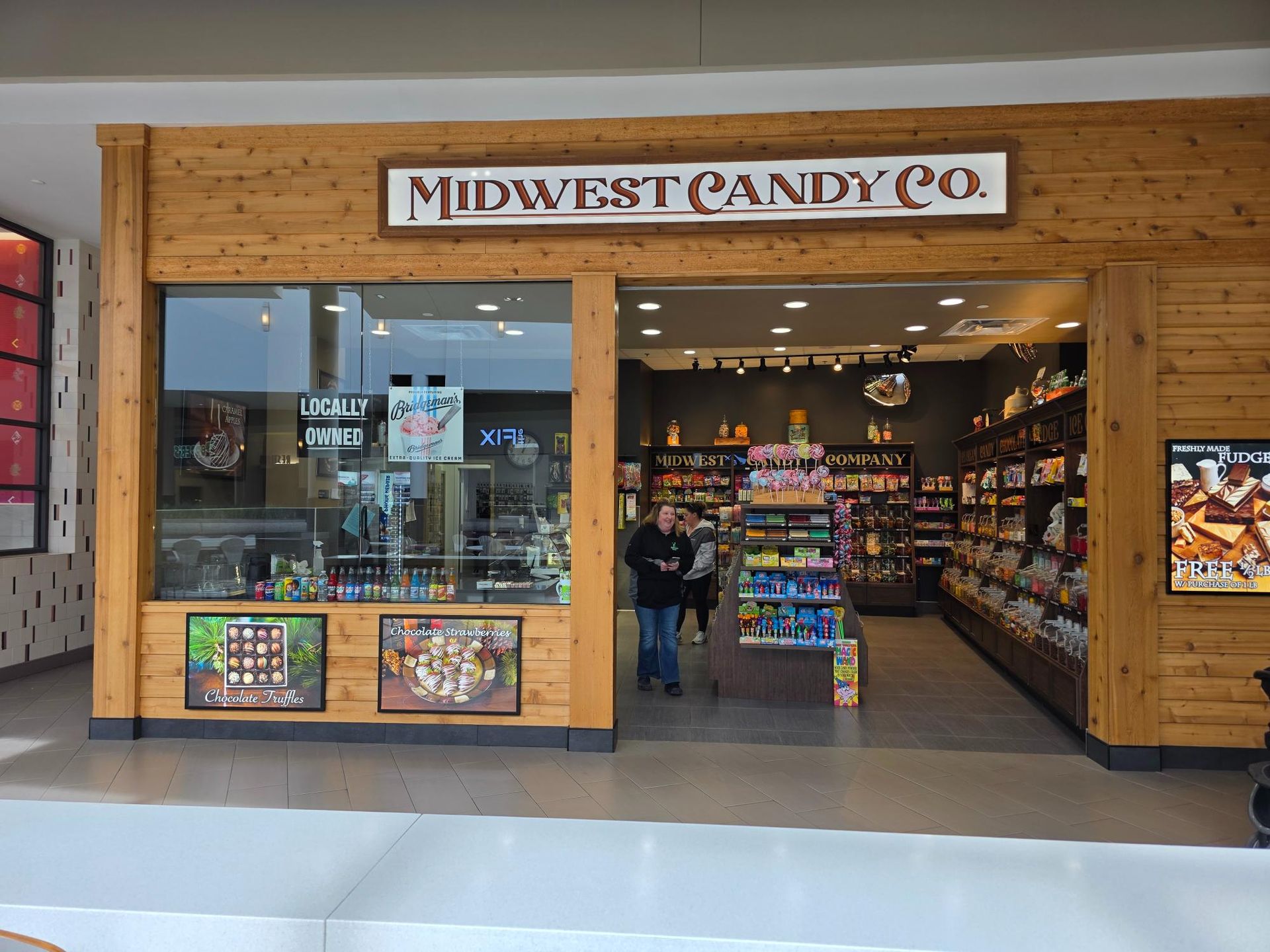 Midwest Candy Co. storefront with wooden facade, glass windows, and a person entering. Inside, shelves stocked with candy.