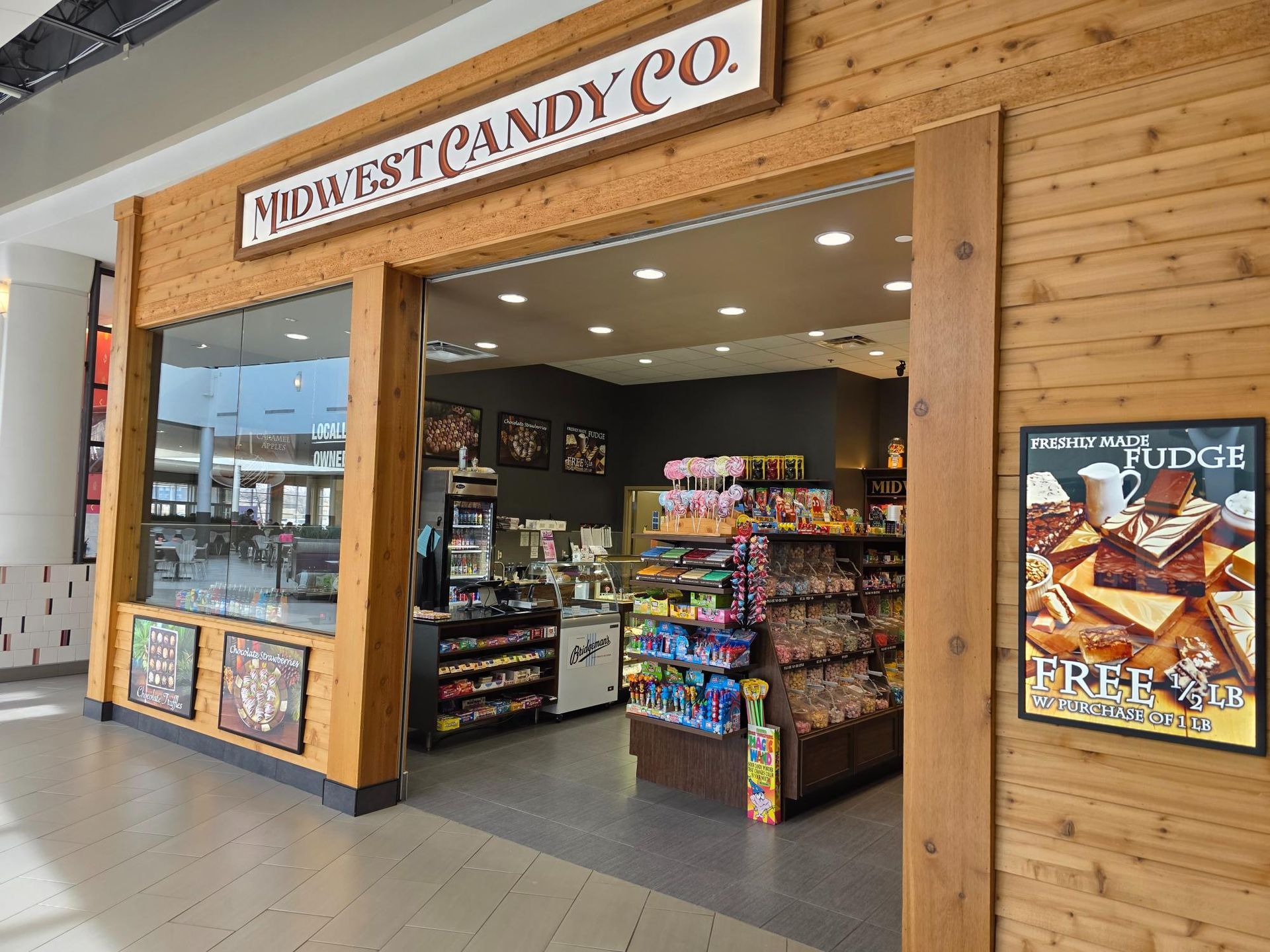 Midwest Candy Co. store front; wood siding, open door, shelves of candy, poster for fudge.