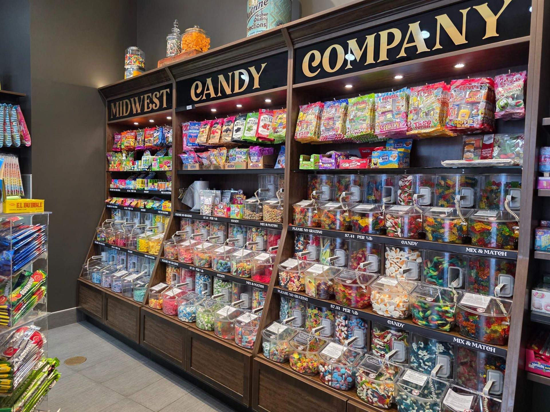 Candy store shelves stocked with various candies, labeled 