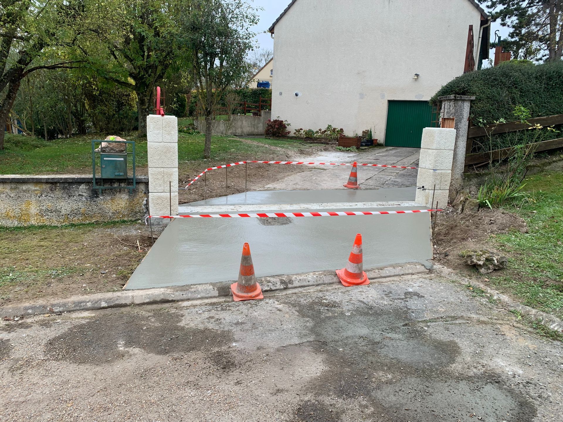 Allée en béton fraîchement coulée, avec des cônes orange et du ruban adhésif rouge et blanc à l'entrée.