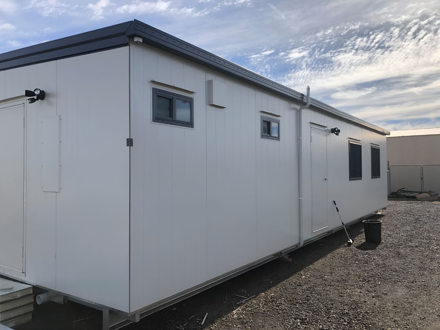 A Large White Building With a Black Roof is Parked in a Gravel Lot — OSM Transportables In Forbes, NSW
