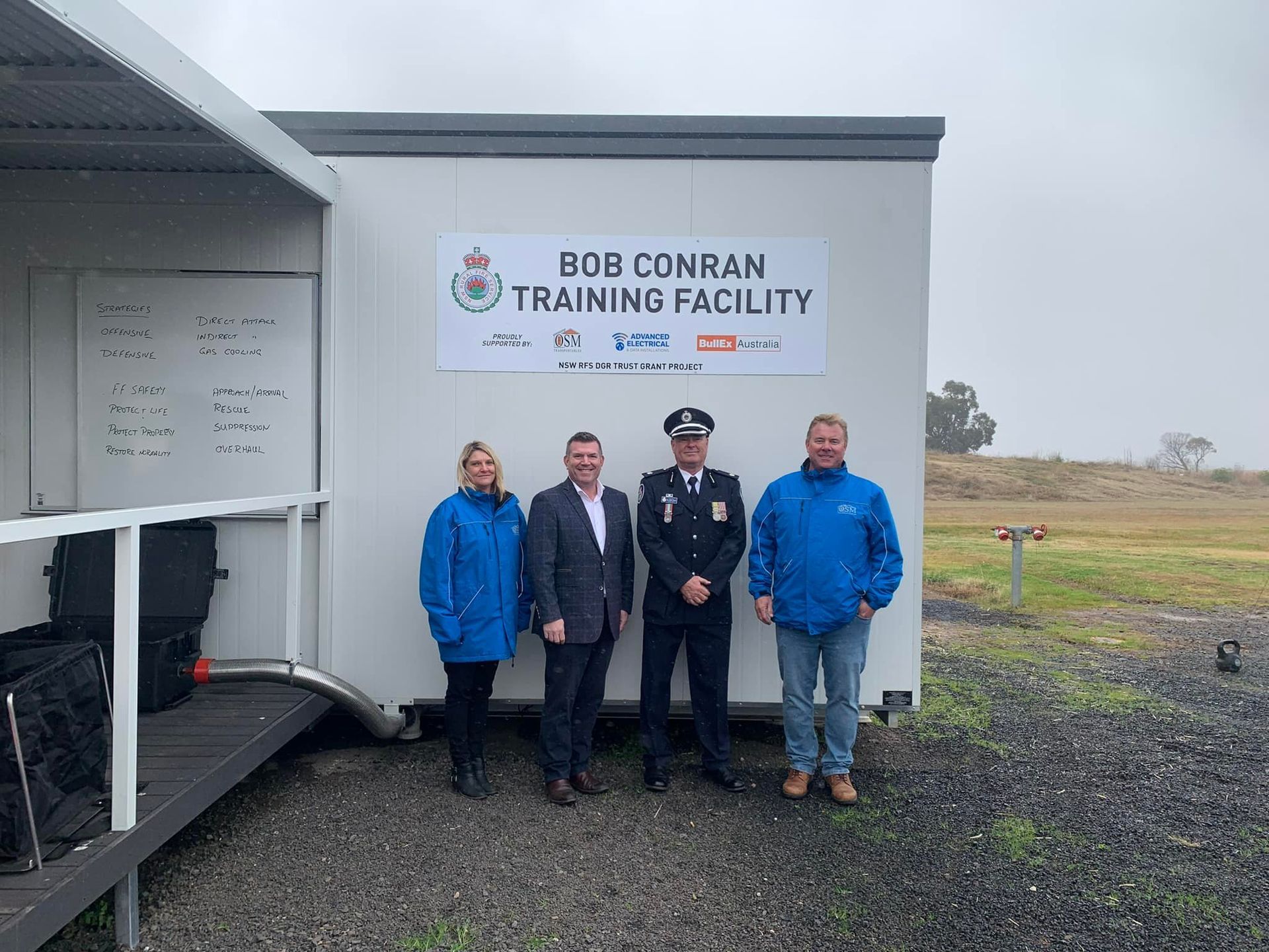 Four People Stand in Front of the Bob Conran Training Facility Building — OSM Transportables In Dubbo, NSW
