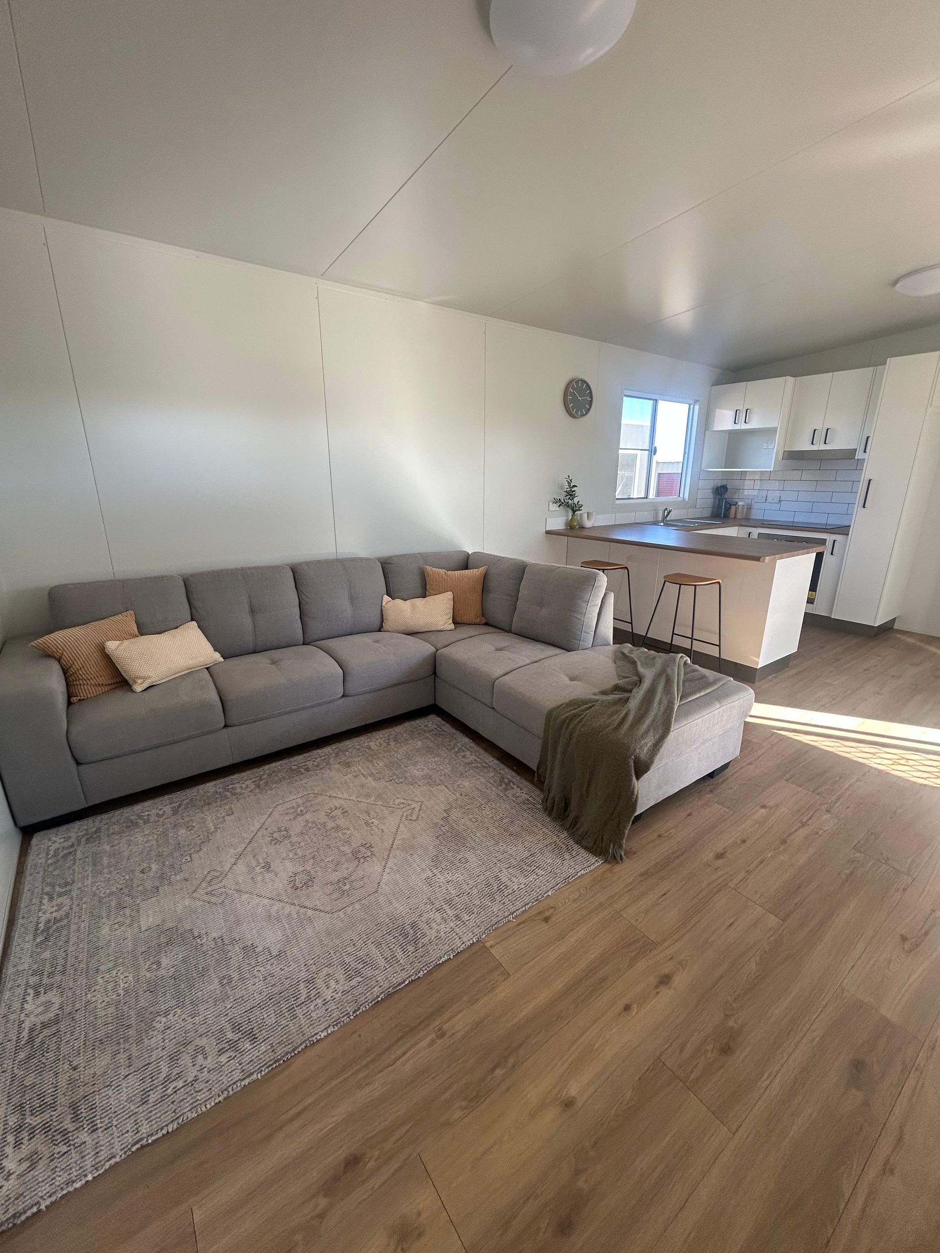 A Grey Sectional Sofa Sits on a Textured Rug in a Living Room Next to an Open Kitchen — OSM Transportables In Dubbo, NSW