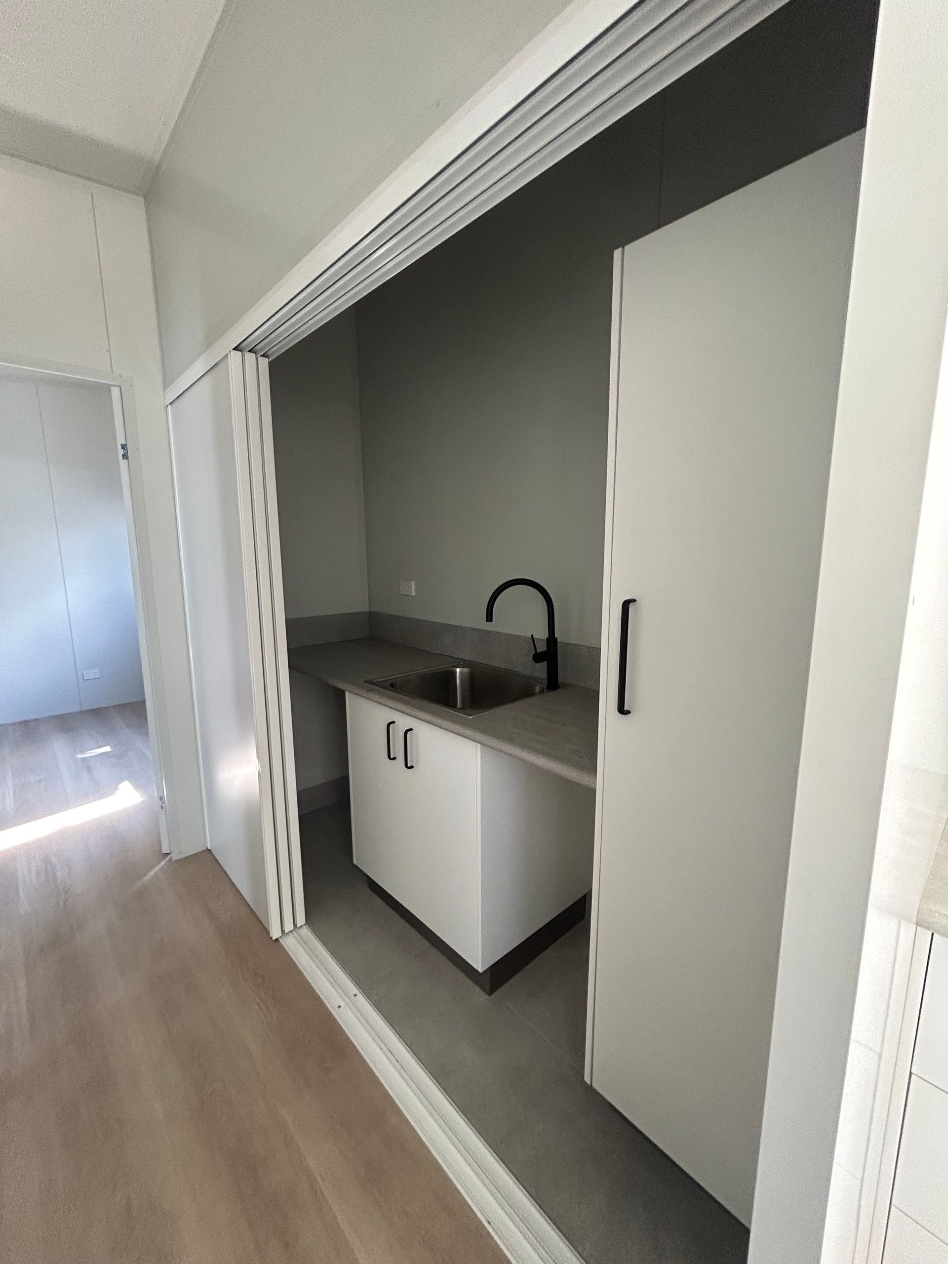 A Small, Enclosed Kitchenette With White Cabinets, a Grey Countertop, and a Black Faucet — OSM Transportables In Dubbo, NSW
