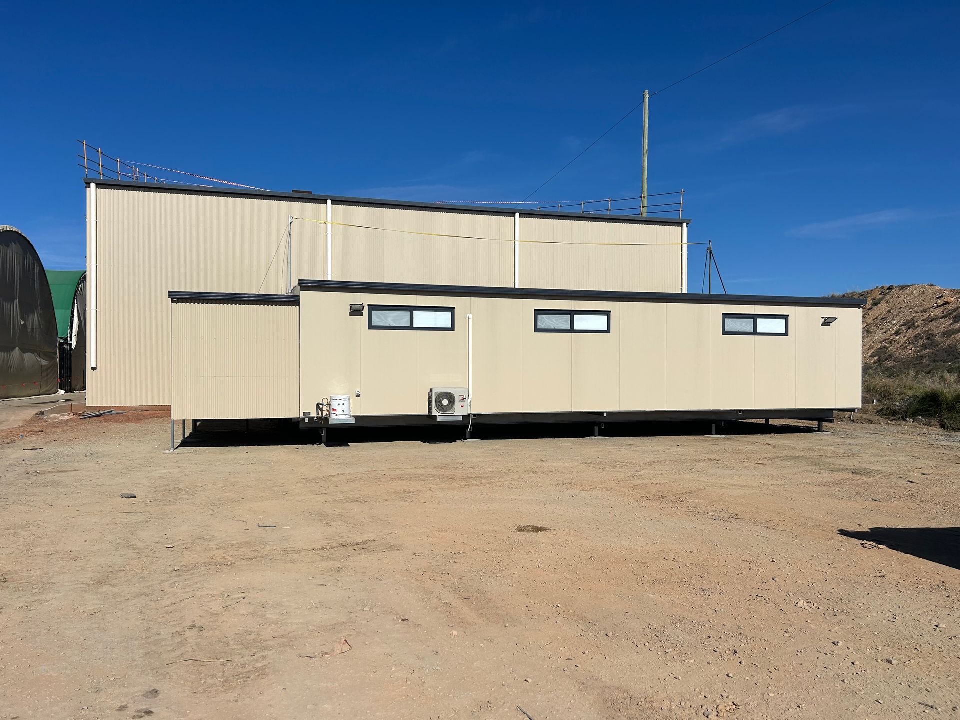 A Beige Modular Office Building Sits on a Dirt Lot Against a Clear Blue Sky — OSM Transportables In Dubbo, NSW