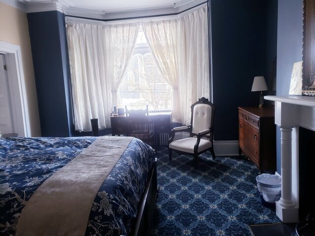 Bedroom with navy blue walls, white curtains, and patterned carpet; bed and antique furniture.