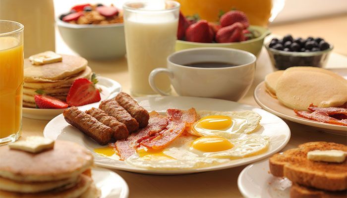 Breakfast spread: pancakes, eggs, bacon, sausage, toast, fruit, orange juice, milk, and coffee.