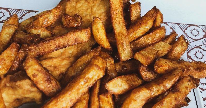 Pile of golden-brown, crispy fried potato wedges on a patterned plate.