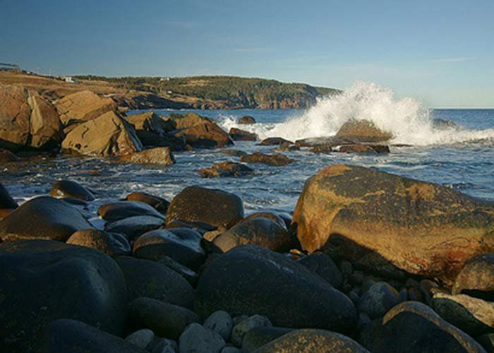 Ocean waves crashing against rocky shoreline. Sunlight illuminates the scene.