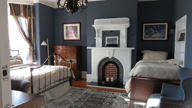 Bedroom with blue walls, two beds, fireplace, antique furniture, and patterned rug.