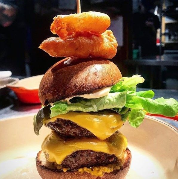 Double-stacked burger with cheese, lettuce, and onion rings, skewered on a plate.