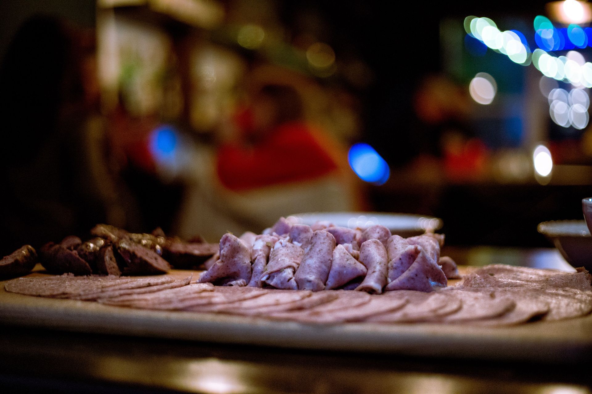 Close-up of sliced meat on a wooden board. Blurred background of a bar with people and lights.