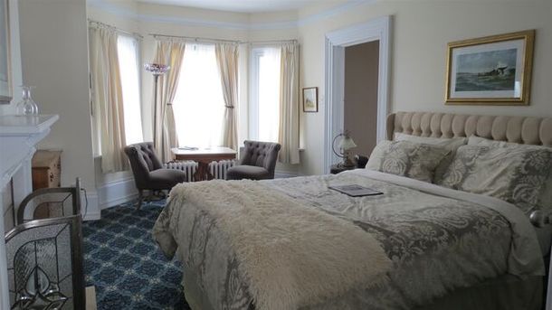 Bedroom with bed, sitting area in bay window, and artwork. Blue carpet, light curtains, and beige bedding.