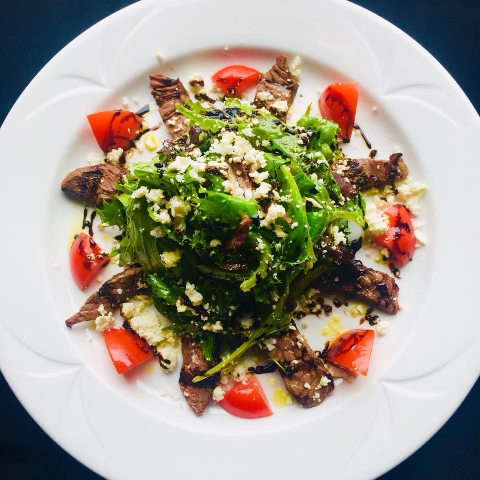 Steak salad with arugula, tomatoes, and crumbled cheese on a white plate.