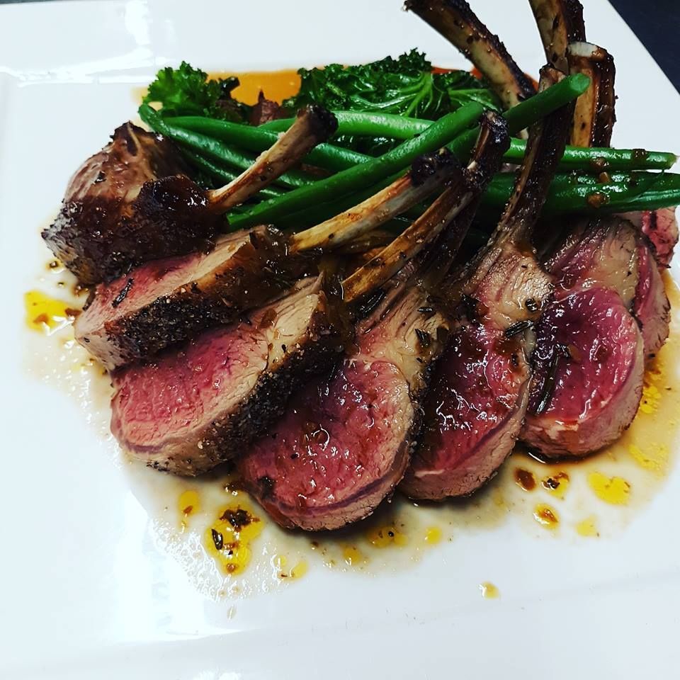 Rack of lamb, sliced, with green beans, and sauce on a white plate.