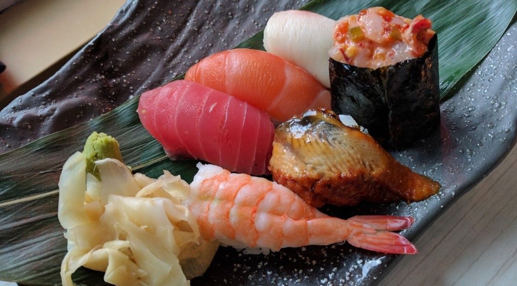 Sushi platter with tuna, salmon, shrimp, and other fish on a black plate.