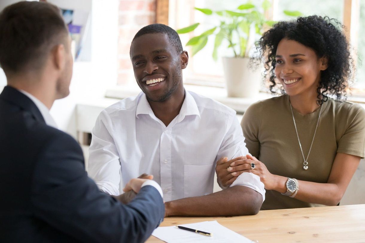 A man and woman are shaking hands with a man in a suit while sitting at a table.