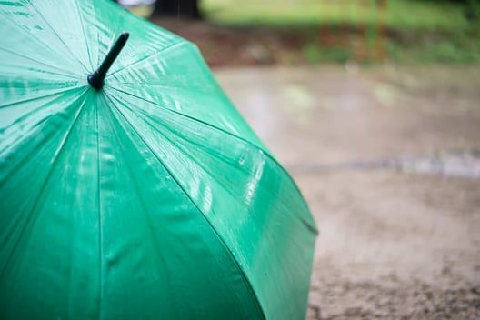 A green umbrella is sitting on the ground in the rain.
