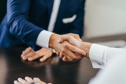 Two men are shaking hands over a table.