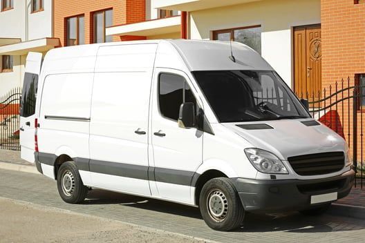 A white van is parked in front of a brick building.