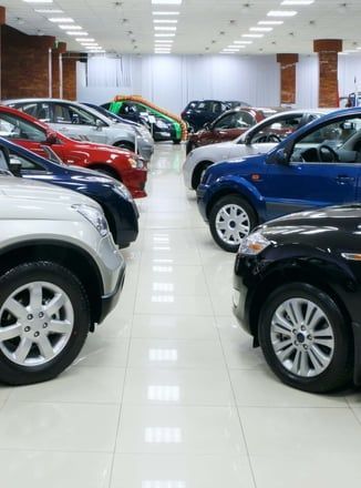 A row of cars are parked in a showroom.