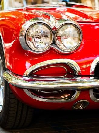 A red car with two headlights is parked on the side of the road.