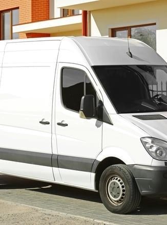 A white van is parked in front of a brick building.