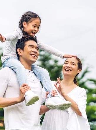 A man is carrying a little girl on his shoulders in a park.