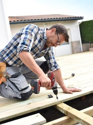 A man is using a drill on a wooden deck.