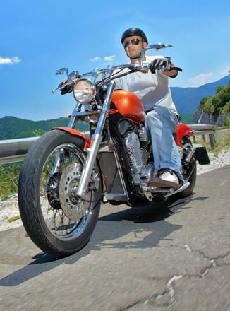 A man is riding an orange motorcycle down a road.