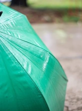 A green umbrella is sitting on the ground in the rain.