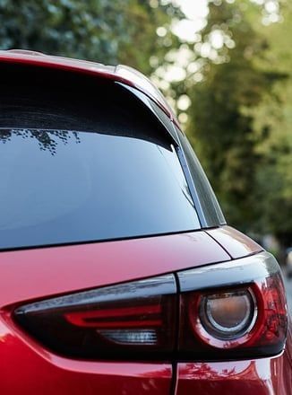 A close up of the back of a red car with trees in the background.