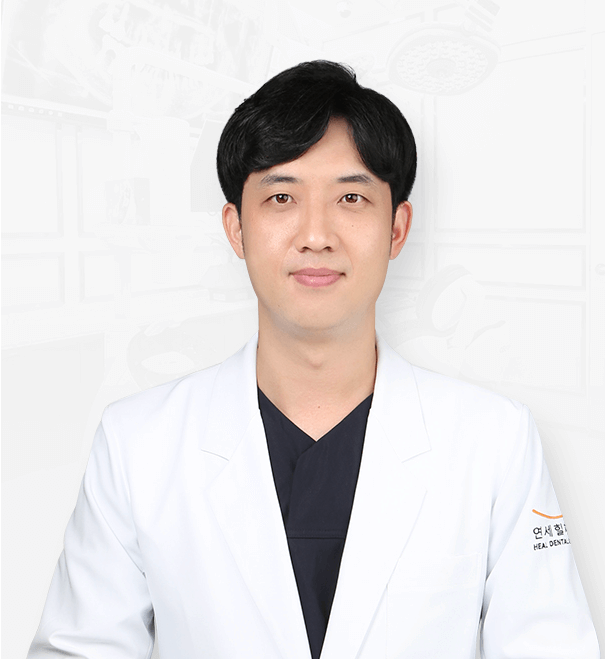 Man in white lab coat, smiling, wearing dark top. Light background.