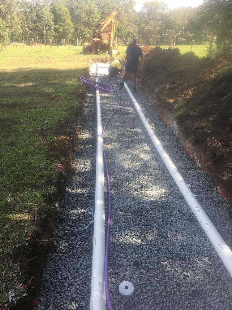 Workers Installing Drainage Pipes in a Gravel-lined Trench — VR Marsden Plumbing in Corindi Beach, NSW