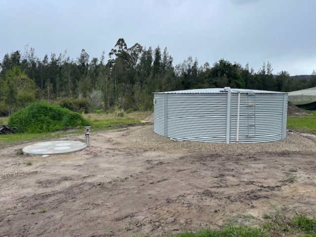 A large metal water tank is sitting on dirt lawn  — VR Marsden Plumbing in Red Rock, NSW