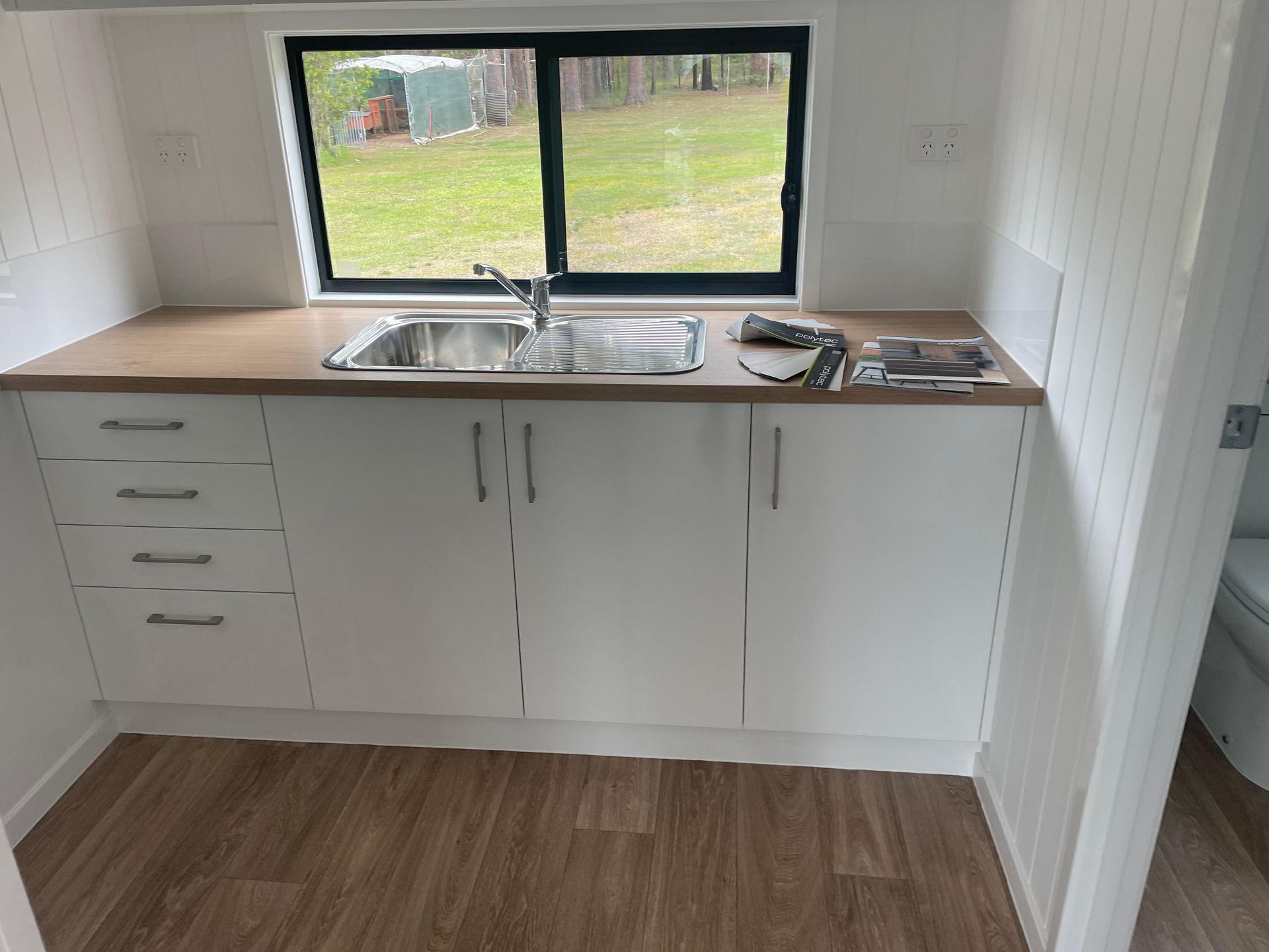Kitchen with white cabinets, stainless steel sink, wood countertop, and window— VR Marsden Plumbing in Red Rock, NSW